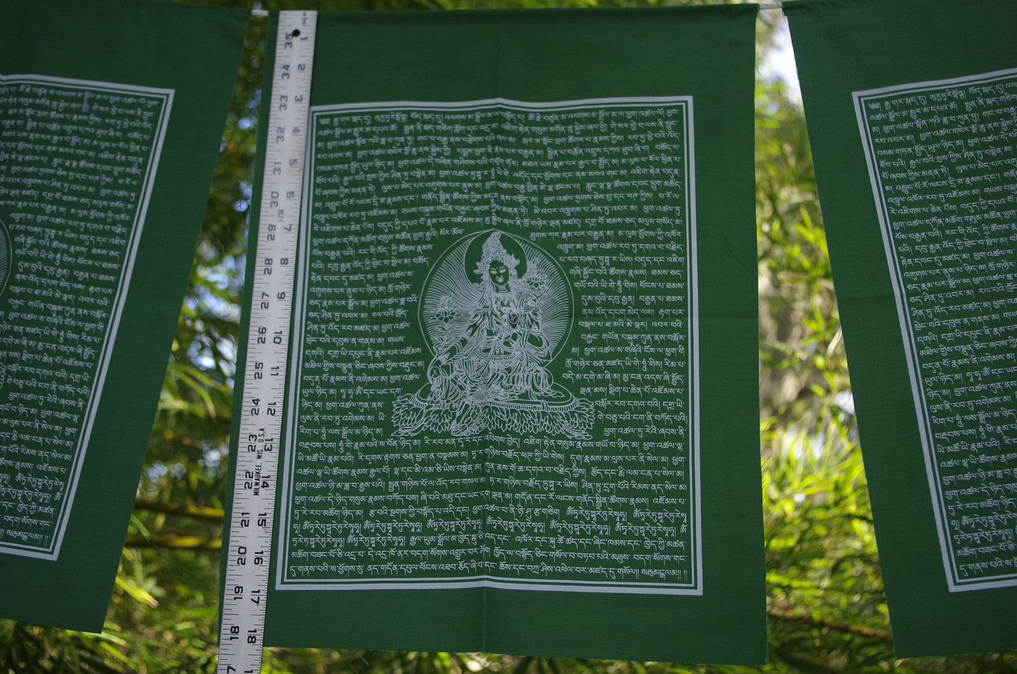 A single flag of high-quality Green Tara Tibetan prayer flags, with white ink on green cloth, each measuring 14x17 inches and hanging outdoors.