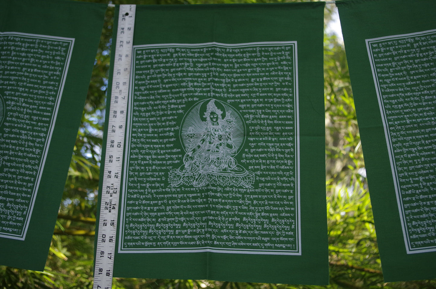A single flag from a 5 flag strand of high-quality Green Tara Tibetan prayer flags, with white ink on green cloth, each measuring 14x17 inches and hanging outdoors.