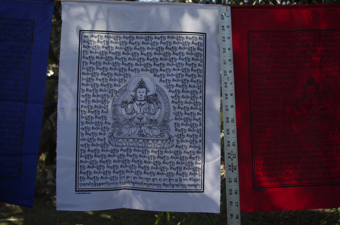 A detail of a single white Chenrezig prayer flags each 14x17 inches, depicting the Buddha of Compassion hanging outdoors.