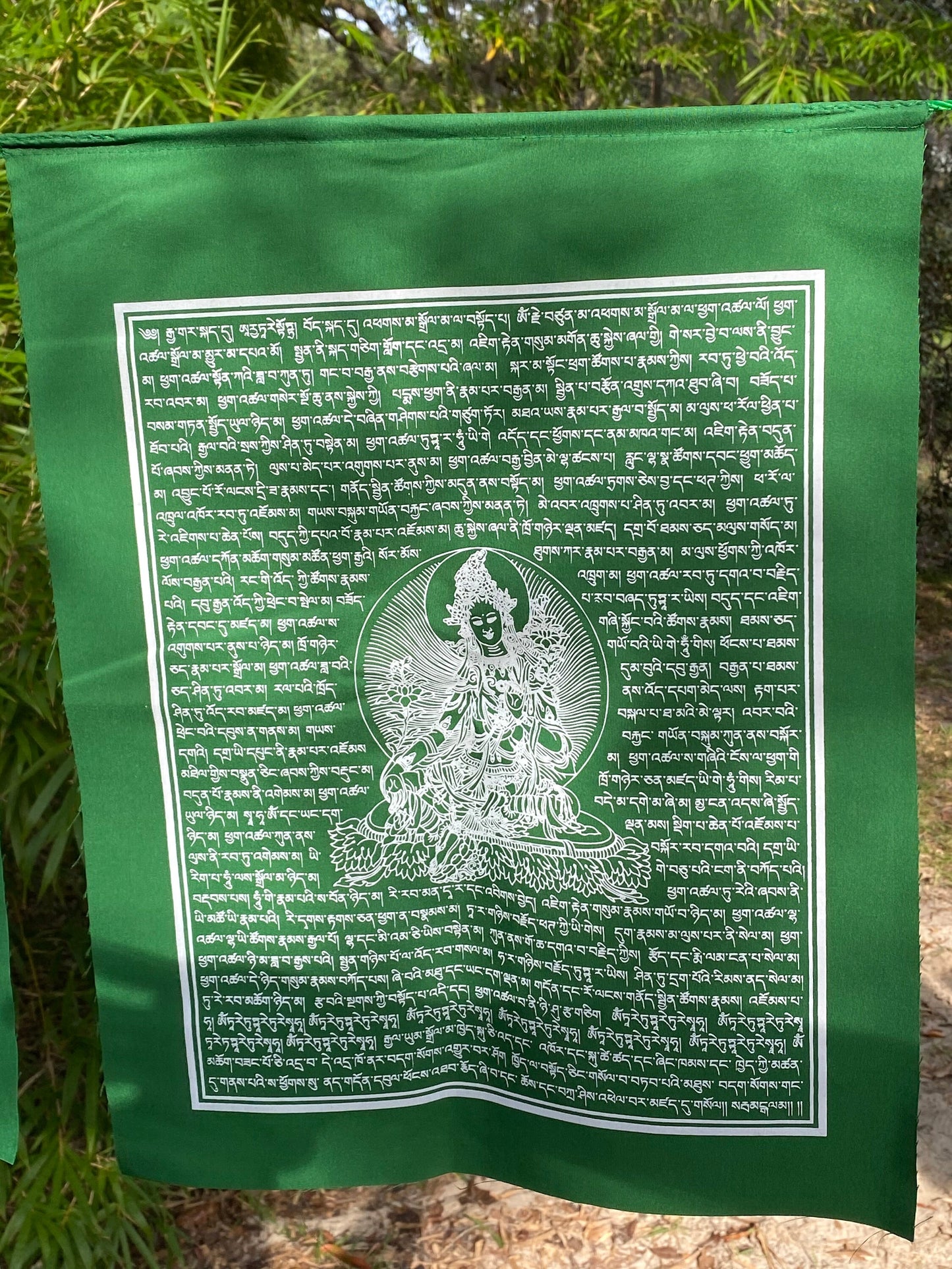 A 14x17&quot; Green Tara prayer flag, printed in white ink on green cloth. Part of a set of 25 high-quality flags, hanging outdoors
