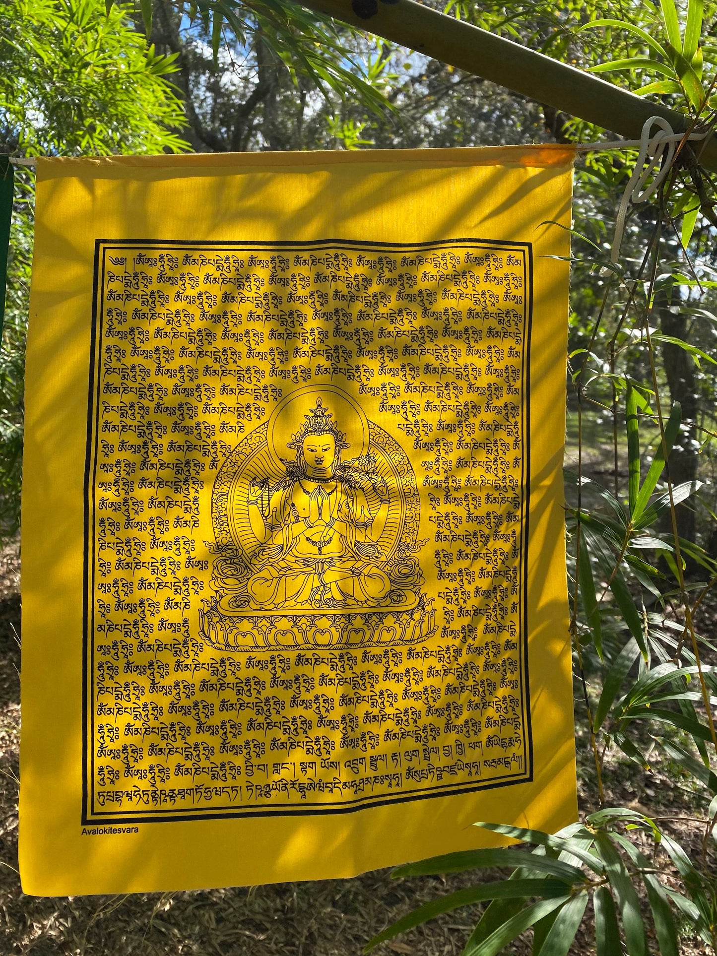 A close up of 1 yellow Chenrezig prayer flag in 5 colors, each 14x17 inches, depicting the Buddha of Compassion hanging outdoors.
