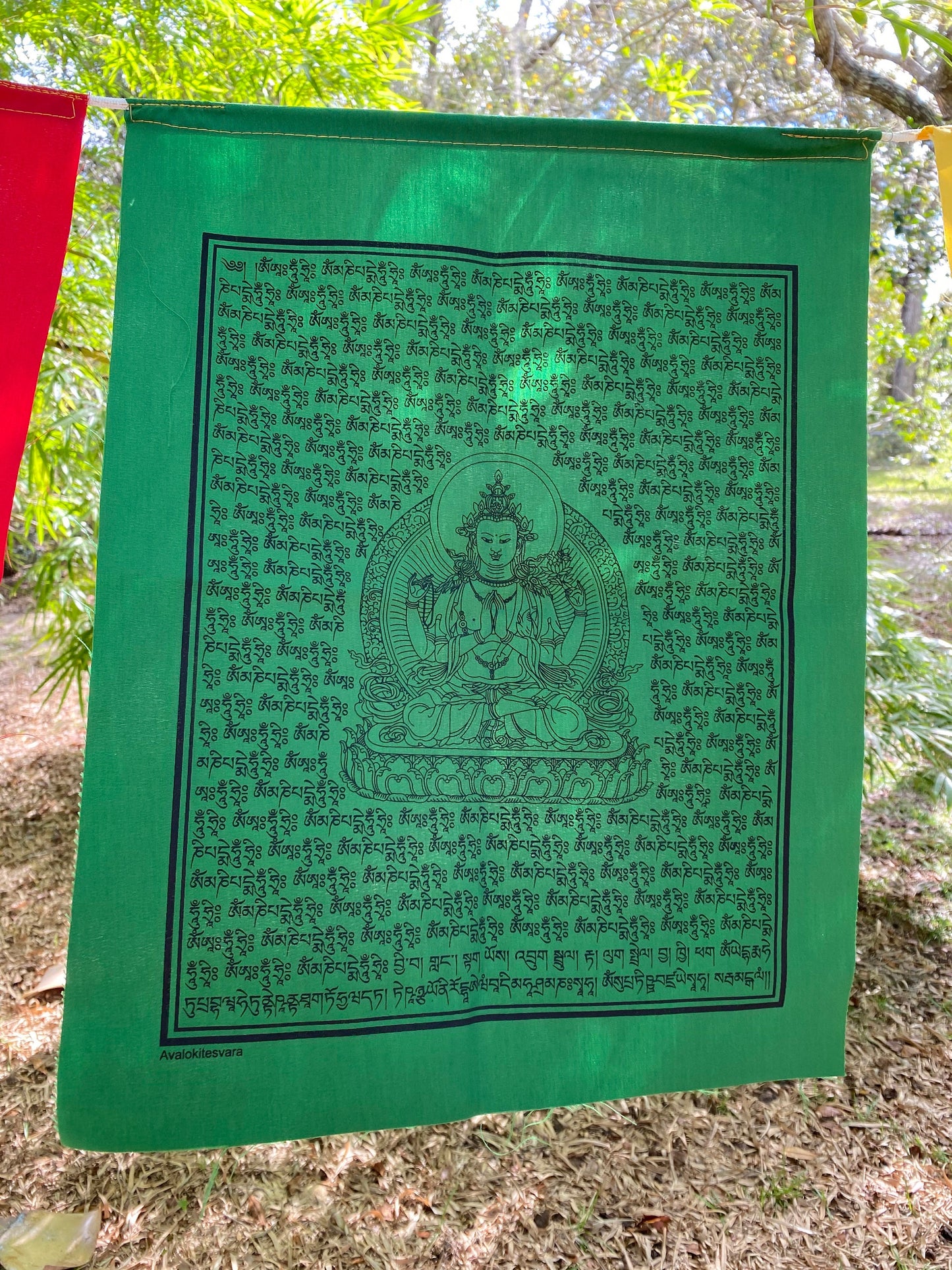 A close up of a single green 14 by 17 inch Chenrezig, Buddha of Compassion, prayer flag hanging outside.