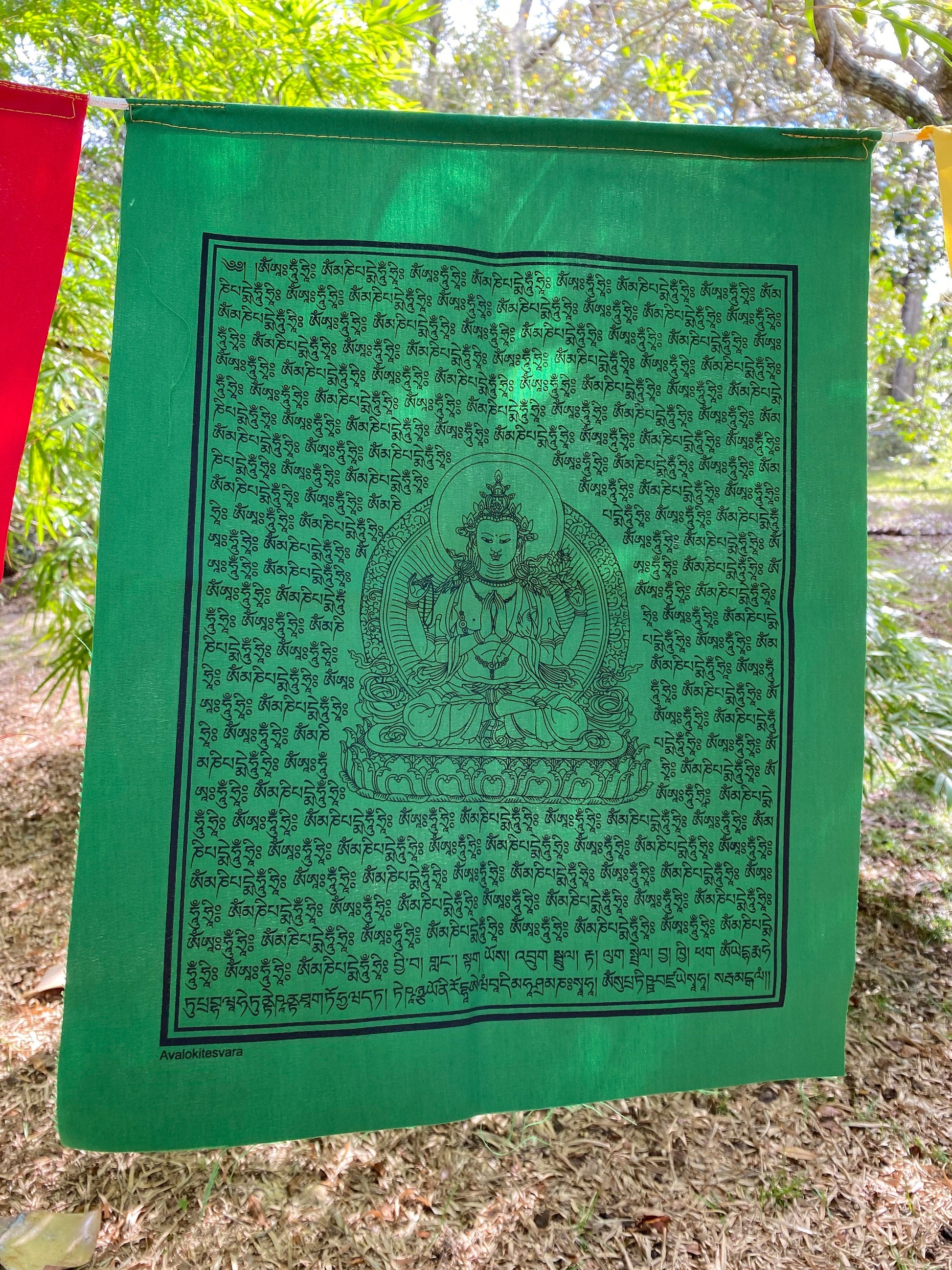 A close up of 1 green Chenrezig prayer flag in 5 colors, each 14x17 inches, depicting the Buddha of Compassion hanging outdoors.