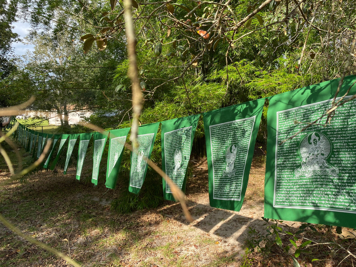 A series of high-quality Green Tara Tibetan prayer flags, with white ink on green cloth, each measuring 14x17 inches and hanging outdoors.