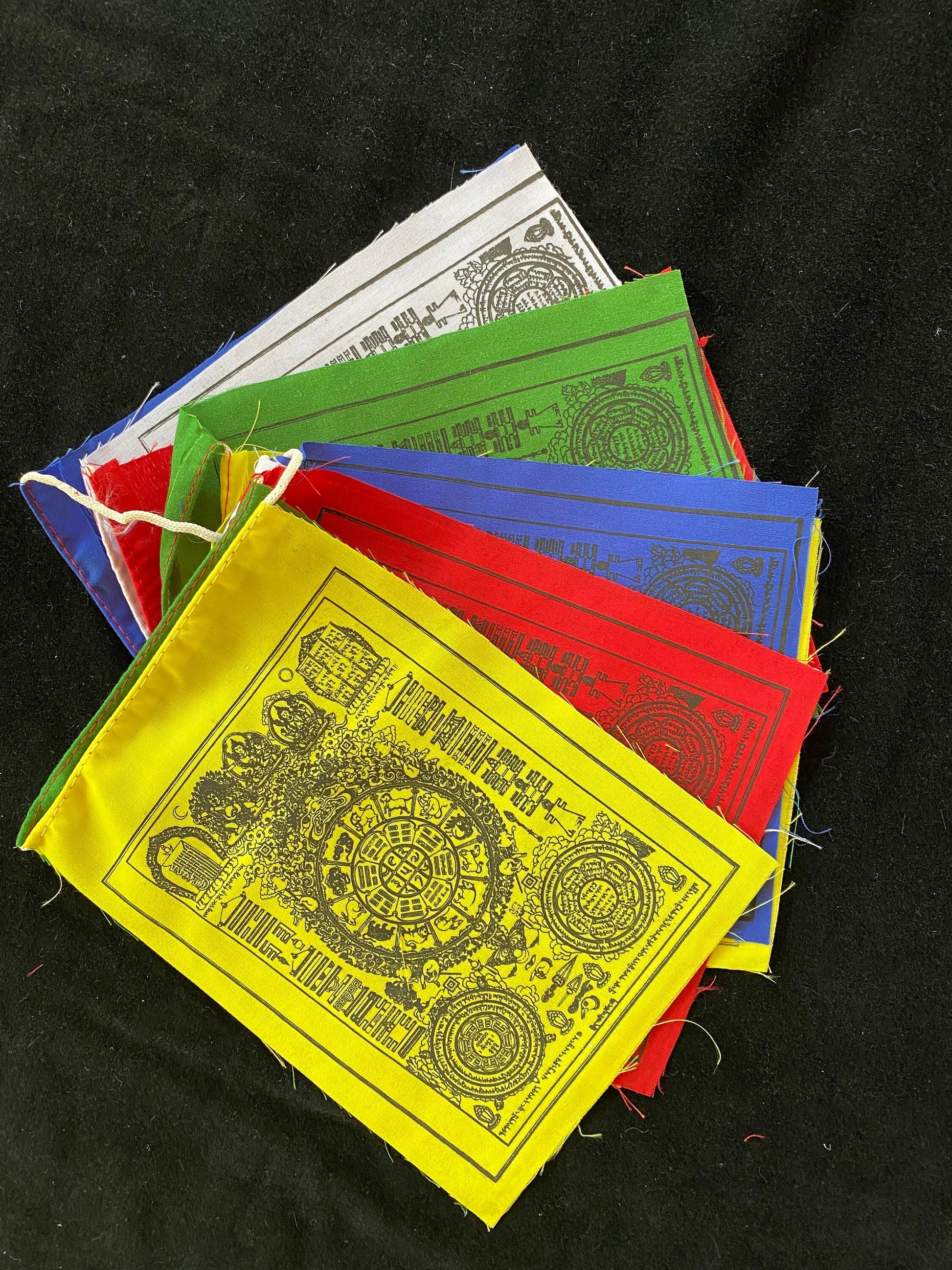 set of 6x7.5 inch Wheel of life prayer flags in 5 colors splayed out against a black background