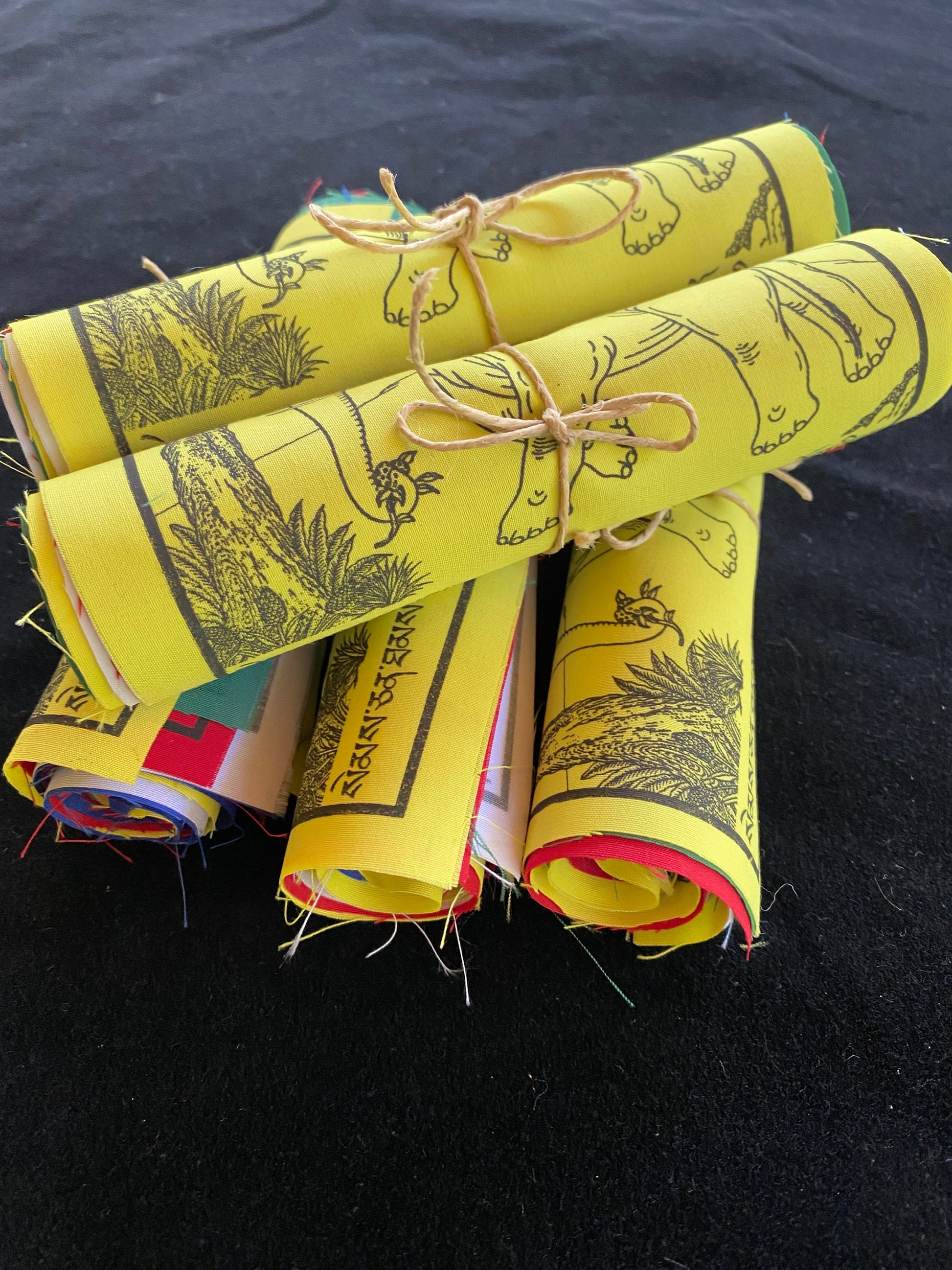 5 offset rolls of 6 inch by 7.5 inch 4 Harmonius Friends prayer flags in five colors stacked on a black background