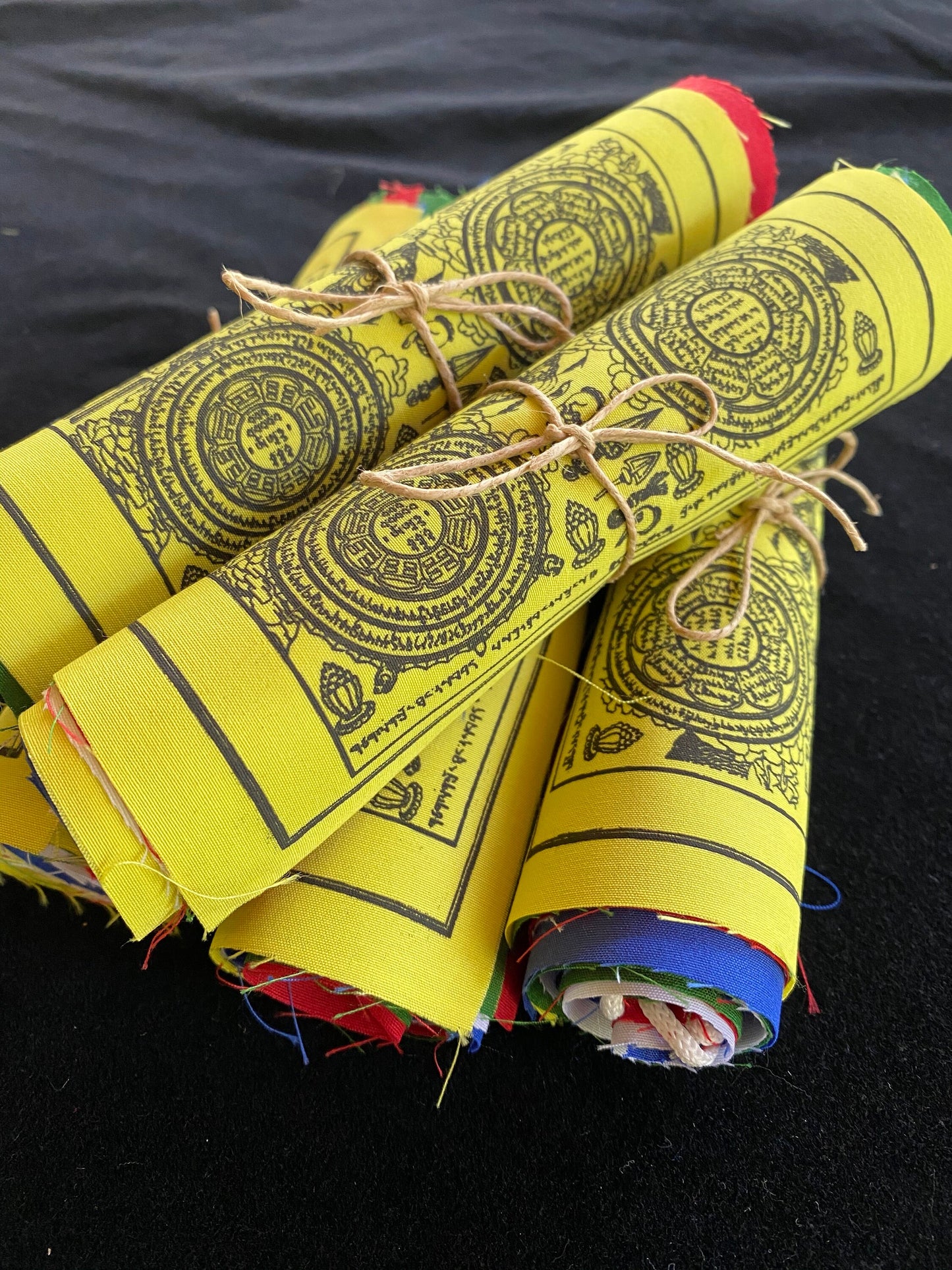 5 rolls of of 6x7.5 inch Wheel of life prayer flags in 5 colors stacked against a black background