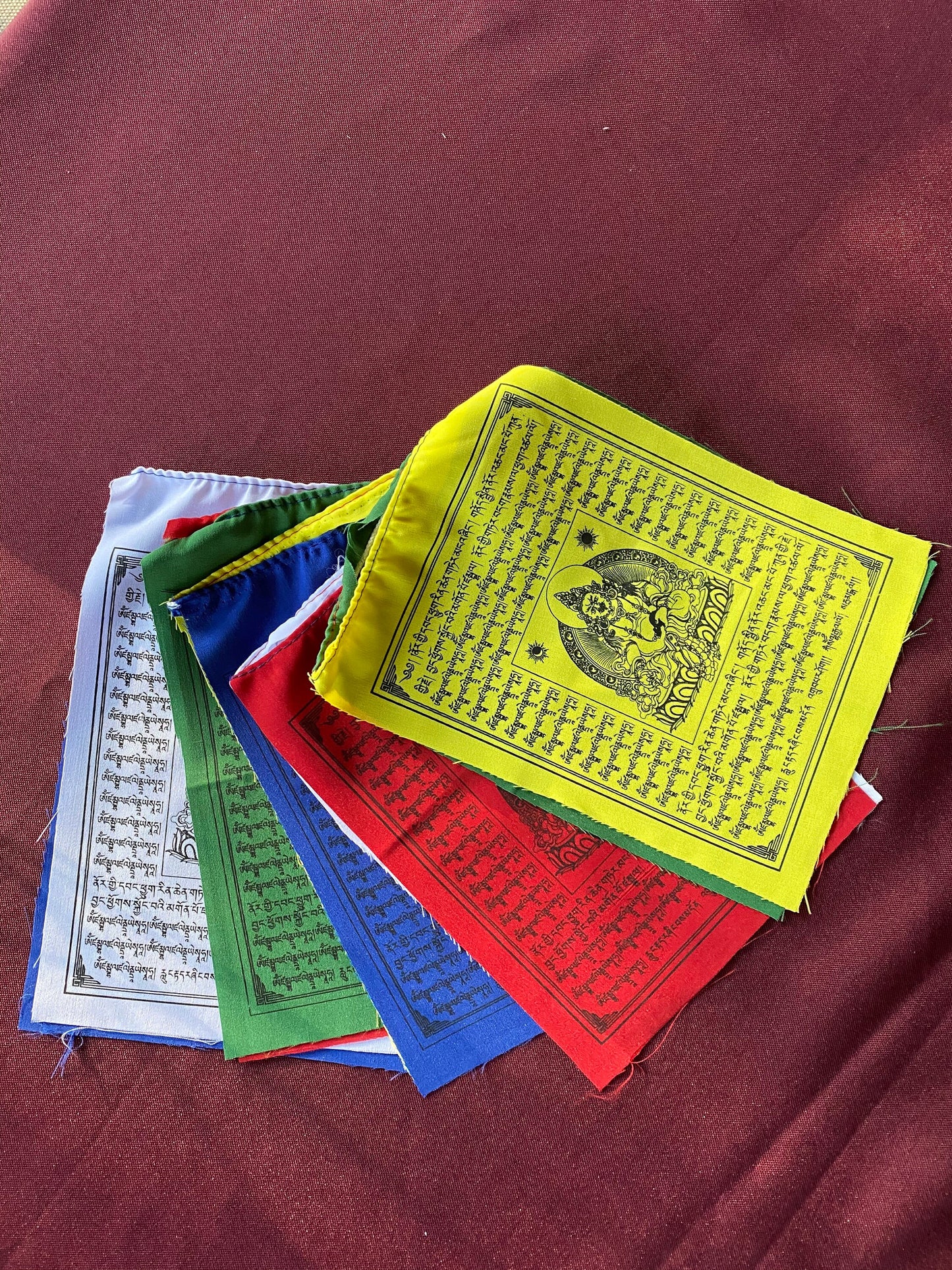 a splayed set 6 inch by 7.5 inch Dzambhala wealth deity prayer flags in five colors set on a medium background
