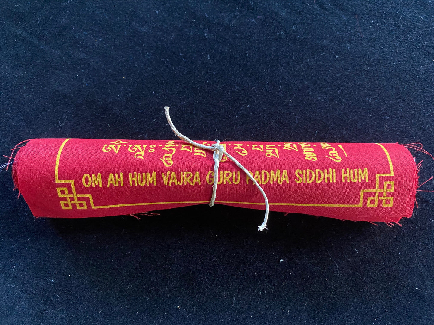 High-quality Tibetan prayer flags: Close-up of 1 rolls of 10 Guru Rinpoche flag sets, 8x8 inches each, colored red, imprinted with his image in yellow ink on a black background.