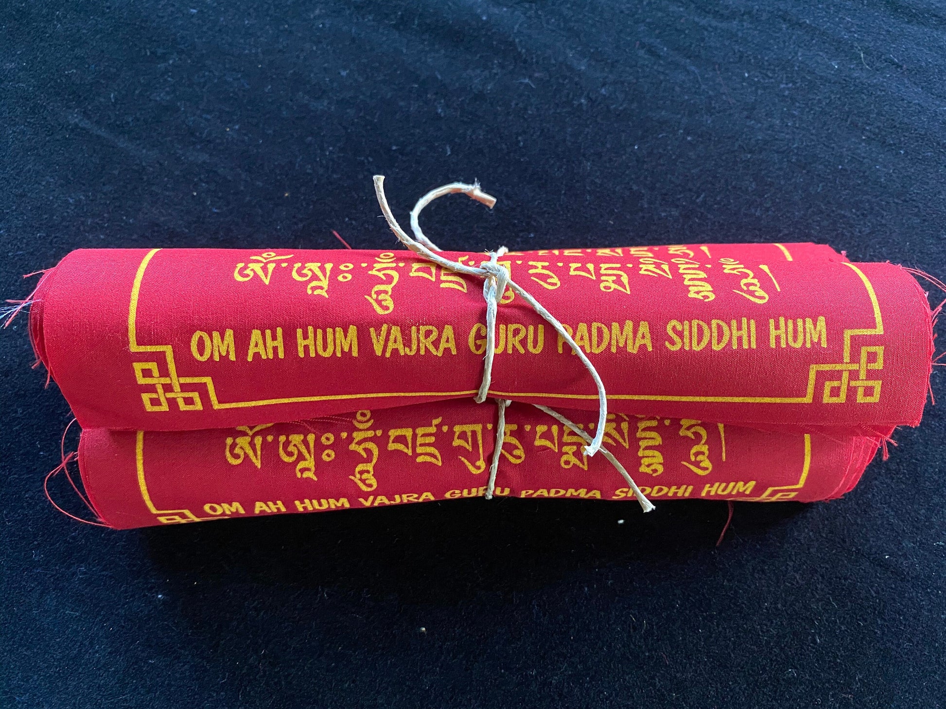 High-quality Tibetan prayer flags: Close-up of 3 rolls of 10 Guru Rinpoche flag sets, 8x8 inches, colored red, imprinted with his image in yellow ink on a black background.