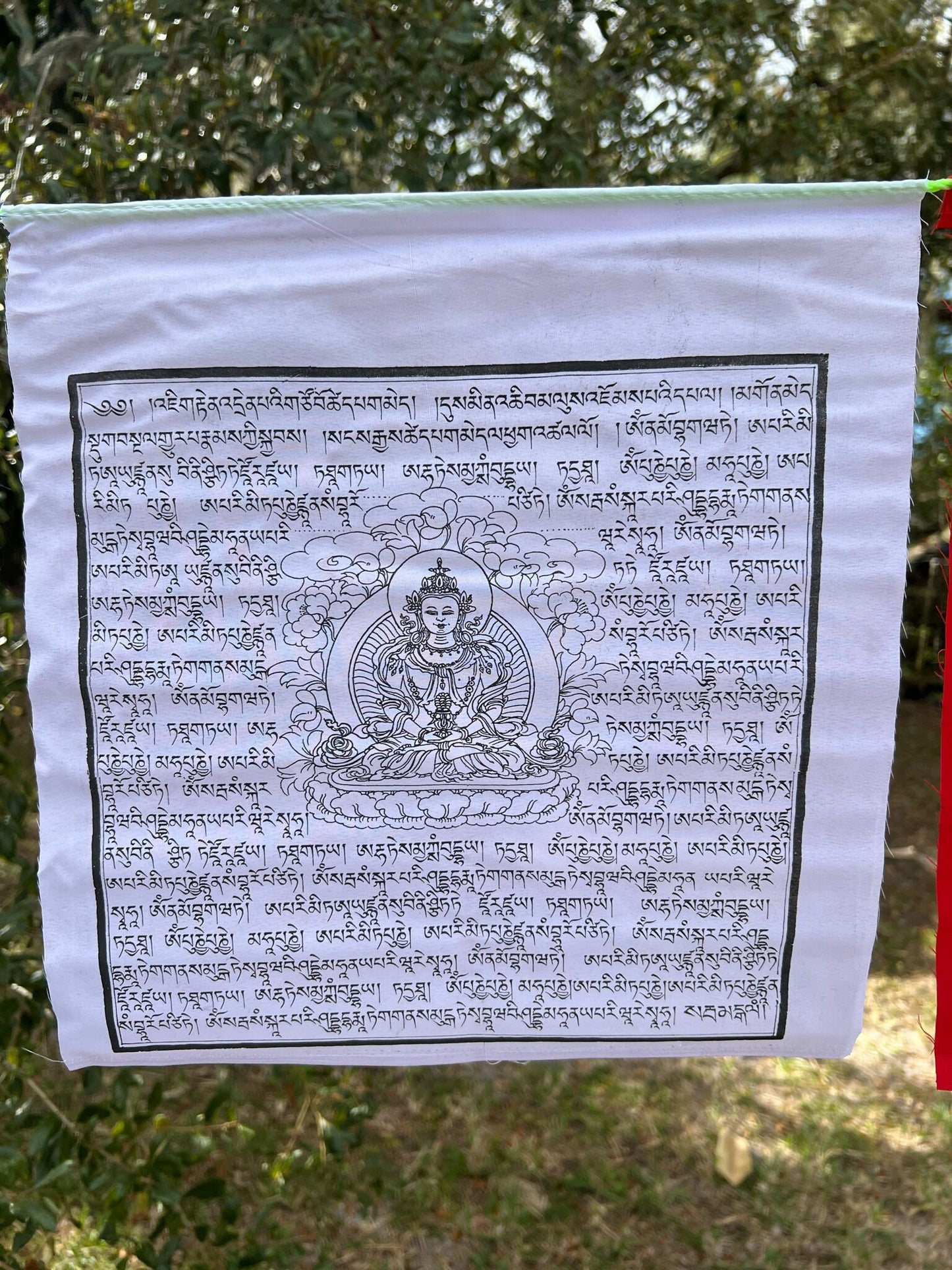 Close-up of white Amitayus flag from a set of 25, featuring central deity image surrounded by Tibetan prayers, symbolizing purity and longevity.